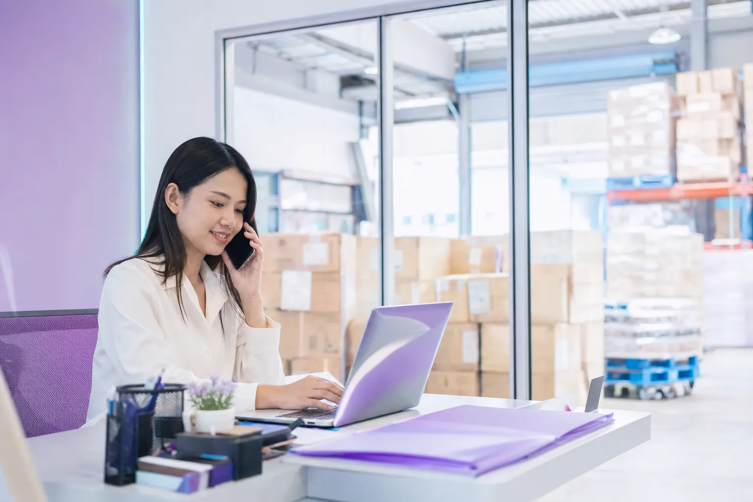 A sales coordinator on a call in an office next to a warehouse